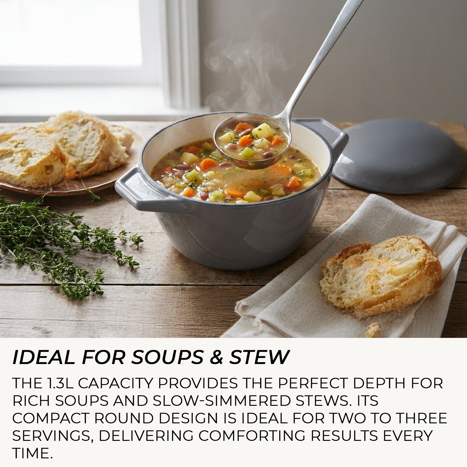 Gray pot of soup with a ladle, bread, and herbs on a wooden table.