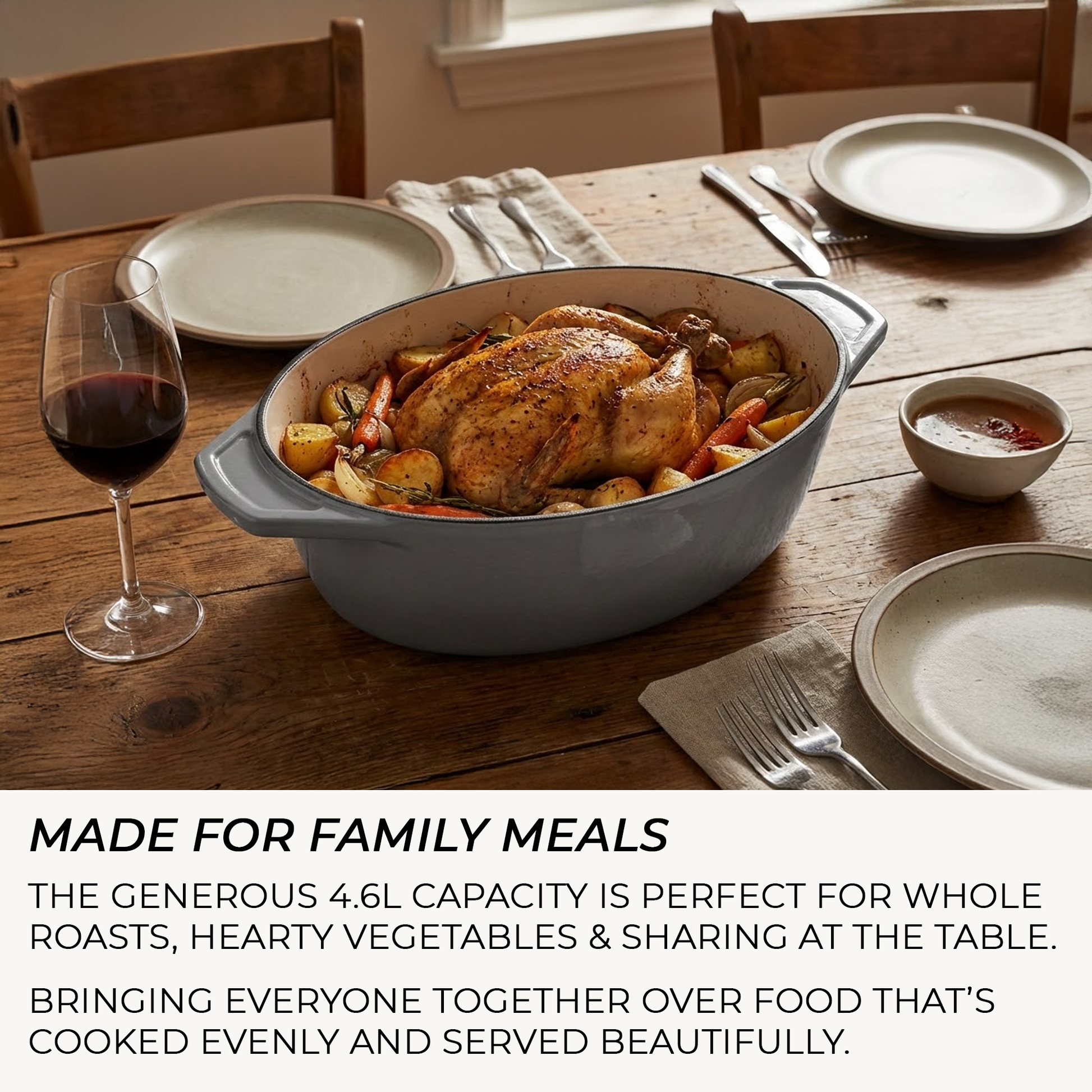 Casserole Dish with roasted chicken and vegetables on a wooden table with plates and wine glasses.