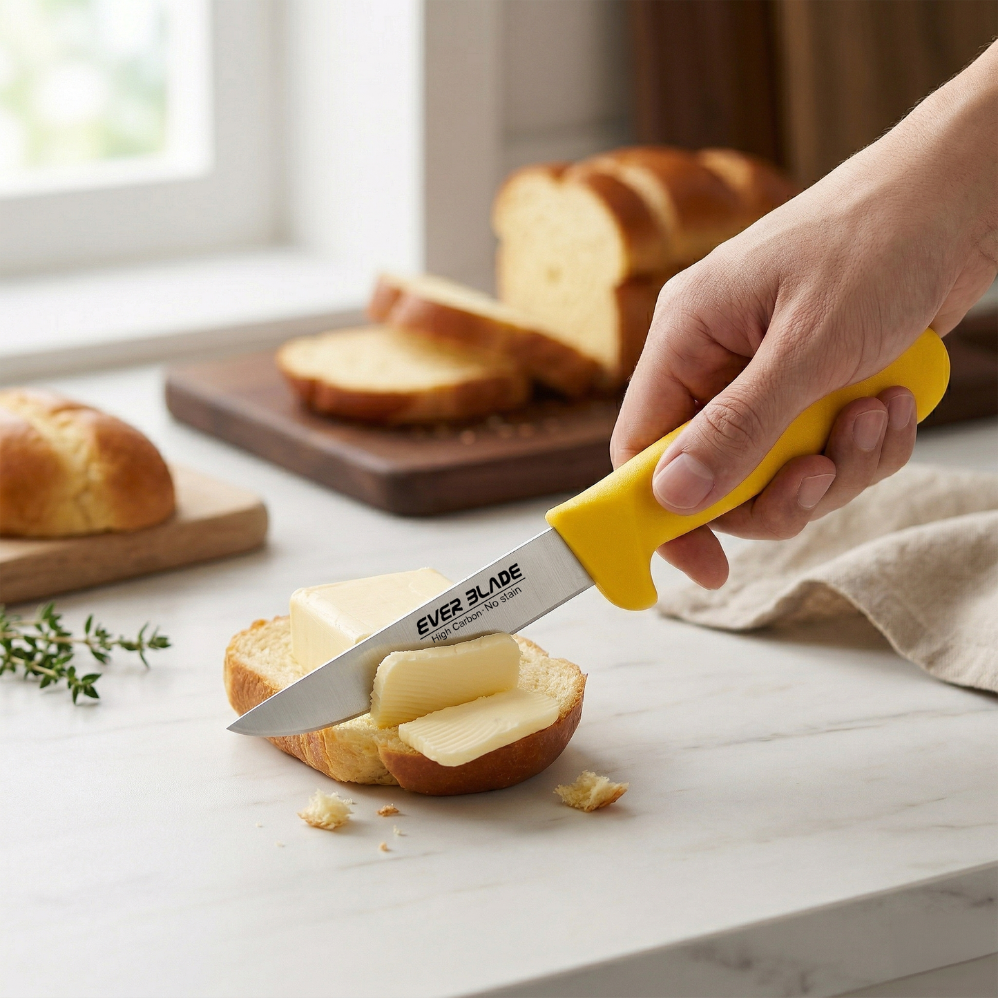 Person spreading butter on a slice of bread using a yellow-handled knife, with more bread slices and a loaf in the background.