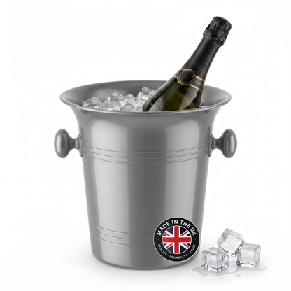 A silver metal champagne bucket filled with ice cubes, with a dark champagne bottle placed inside. The bucket has side handles and a round 'Made in the UK' badge near the bottom front.