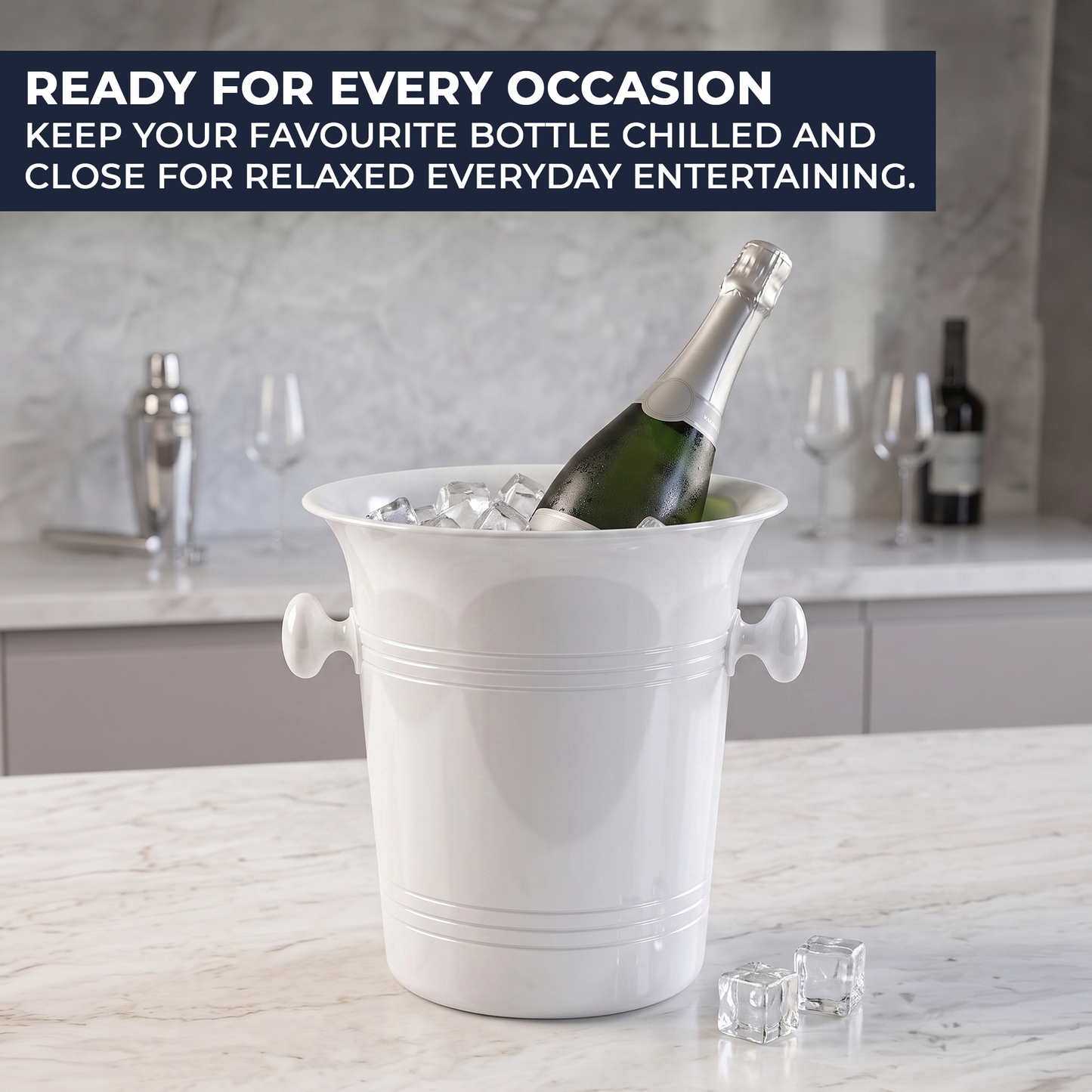 A white champagne bucket filled with ice and a green wine bottle, set on a marble countertop in a kitchen. A dark blue banner at the top reads 'READY FOR EVERY OCCASION KEEP YOUR FAVOURITE BOTTLE CHILLED AND CLOSE FOR RELAXED EVERYDAY ENTERTAINING.
